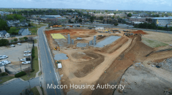 Aerial view of a construction site with dirt mounds, a curved road, and a marina with boats on the left