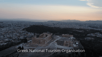 Ancient ruins on a hill above a sprawling city, watermark reads Greek National Tourism Organisation