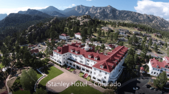 Aerial view of the Stanley Hotel complex with red-roofed buildings, trees, and mountains