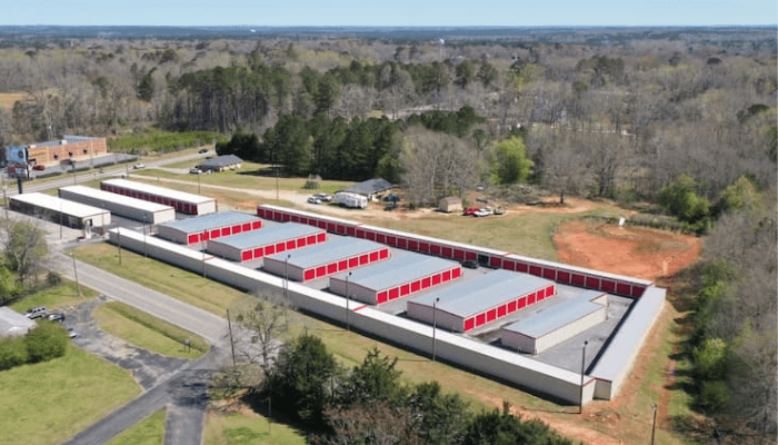 Aerial view of red-door storage units in a long self-storage complex, with trees and roads