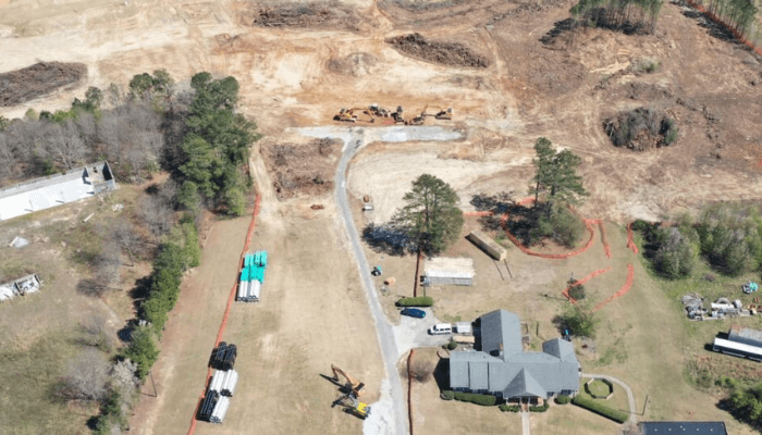 Aerial view of a construction site with dirt roads, yellow excavators, and a gray-roofed building