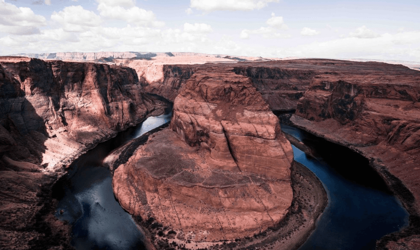 Aerial view of red canyon walls with a winding river looping around a central rock formation