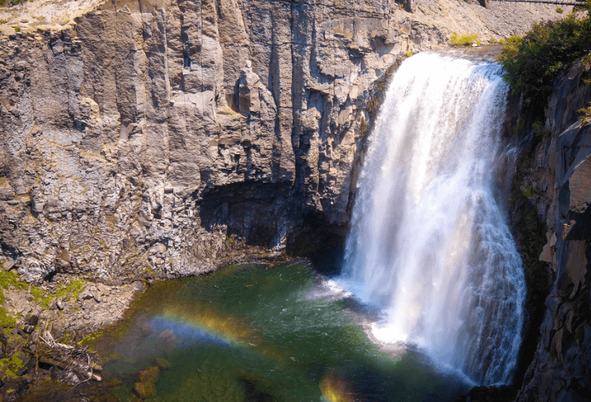 Waterfall cascading down a rocky cliff into a pool with a rainbow in the mist