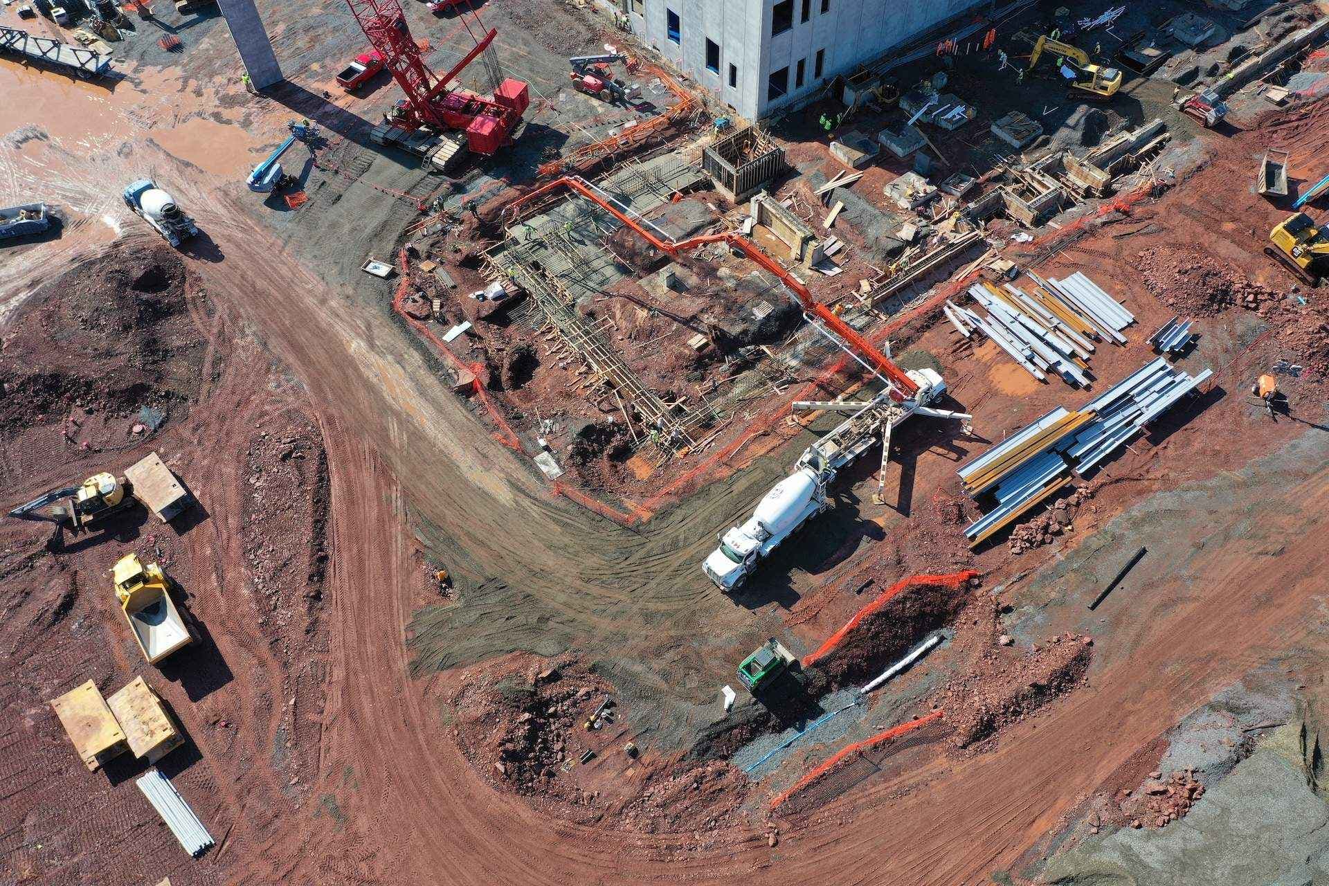 Aerial view of a busy construction site with cranes, concrete forms, and piles of steel