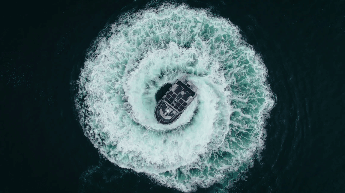 Aerial view of a small boat at the center of a circular wake in dark blue water