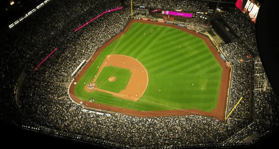 Aerial view of a packed baseball stadium at night, with the diamond, green field, and stands