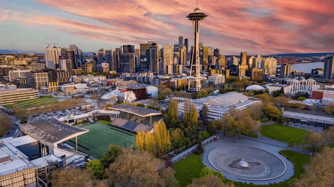 Aerial view of Seattle skyline at sunset with the Space Needle, stadiums, and a circular plaza