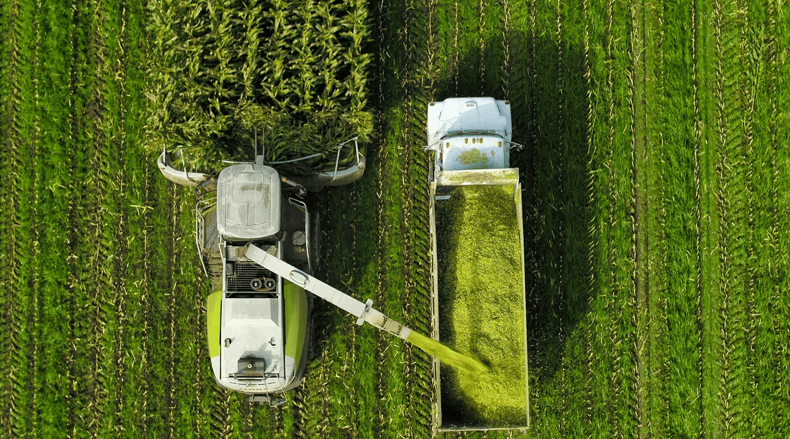 Aerial view of a combine harvester unloading into a trailer pulled by a blue truck in a crop field