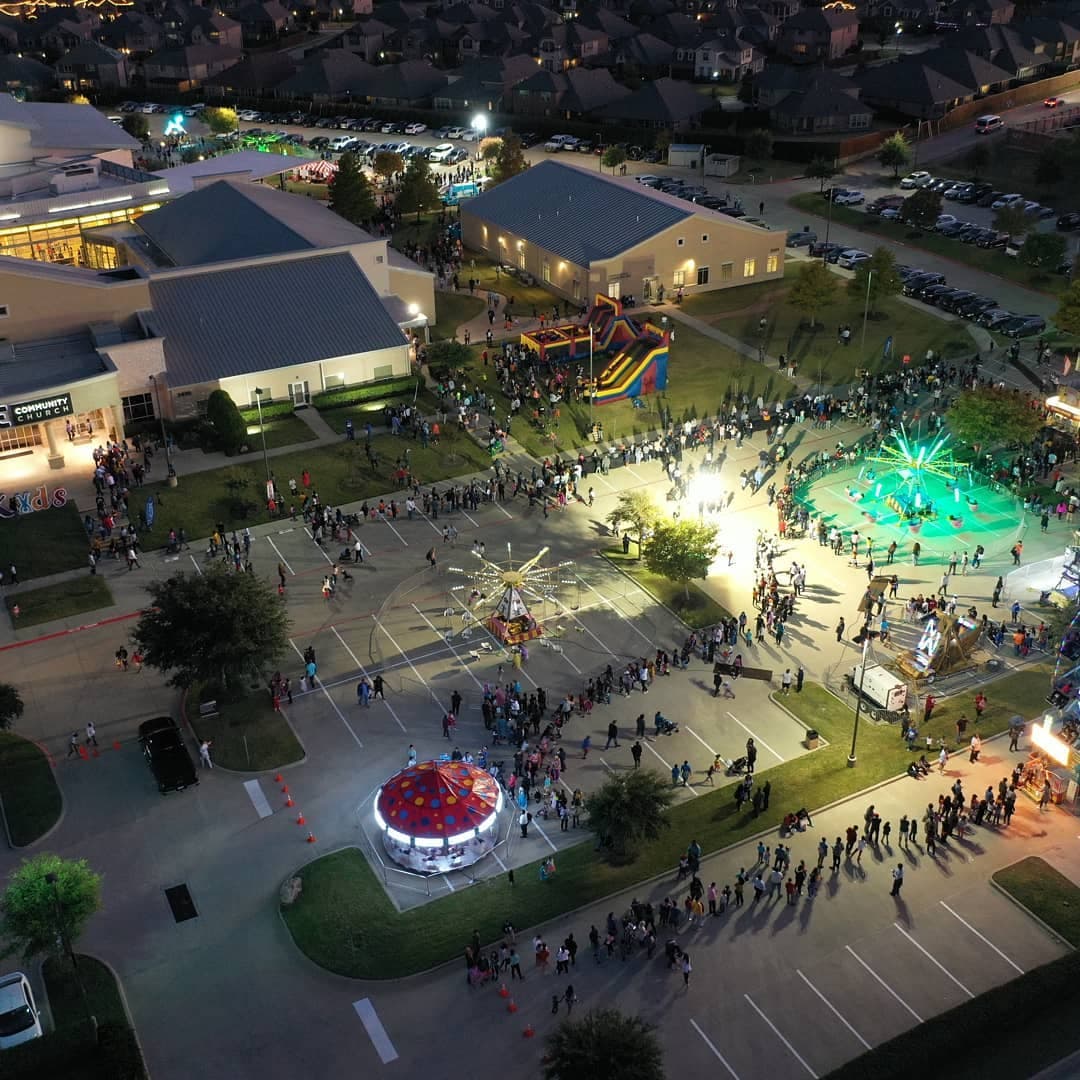 Aerial night view of a crowded campus festival with rides, a colorful inflatable slide, and a round carousel