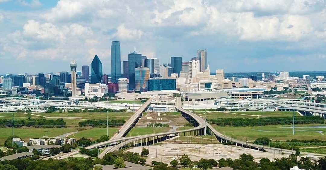 City skyline with tall buildings and a network of elevated highways over green fields