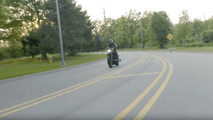 Motorcycle rider wearing a helmet on a curved road with double yellow lines and trees in the background