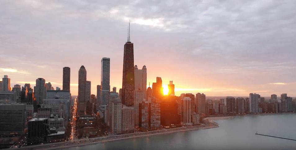 Sunset over a city skyline along the water, tall buildings glow between the towers