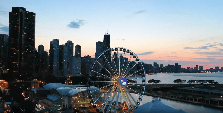 Chicago skyline at sunset with a large illuminated ferris wheel by the lake