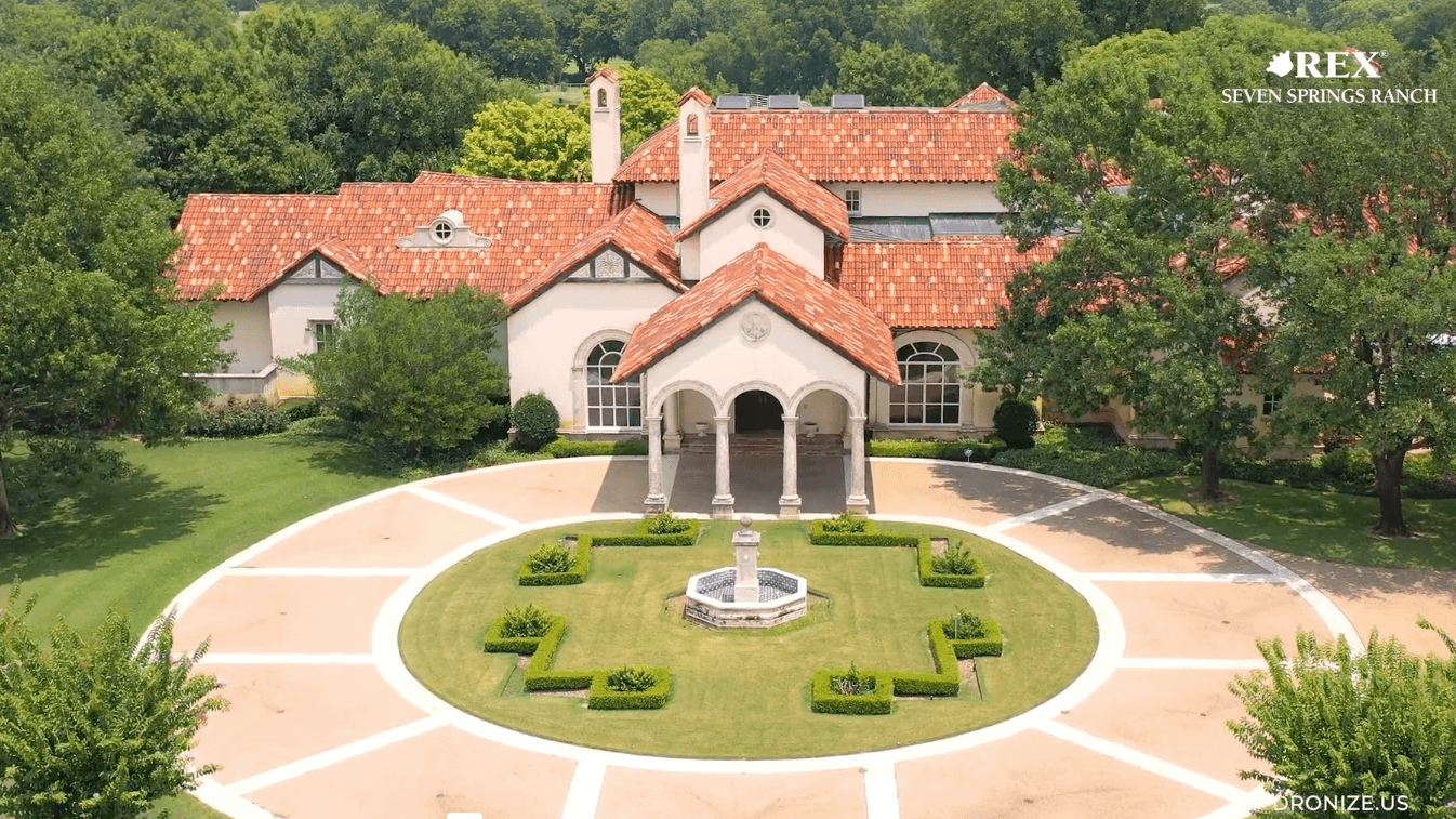 Aerial view of a villa with red tile roof, circular driveway, central fountain, and manicured garden