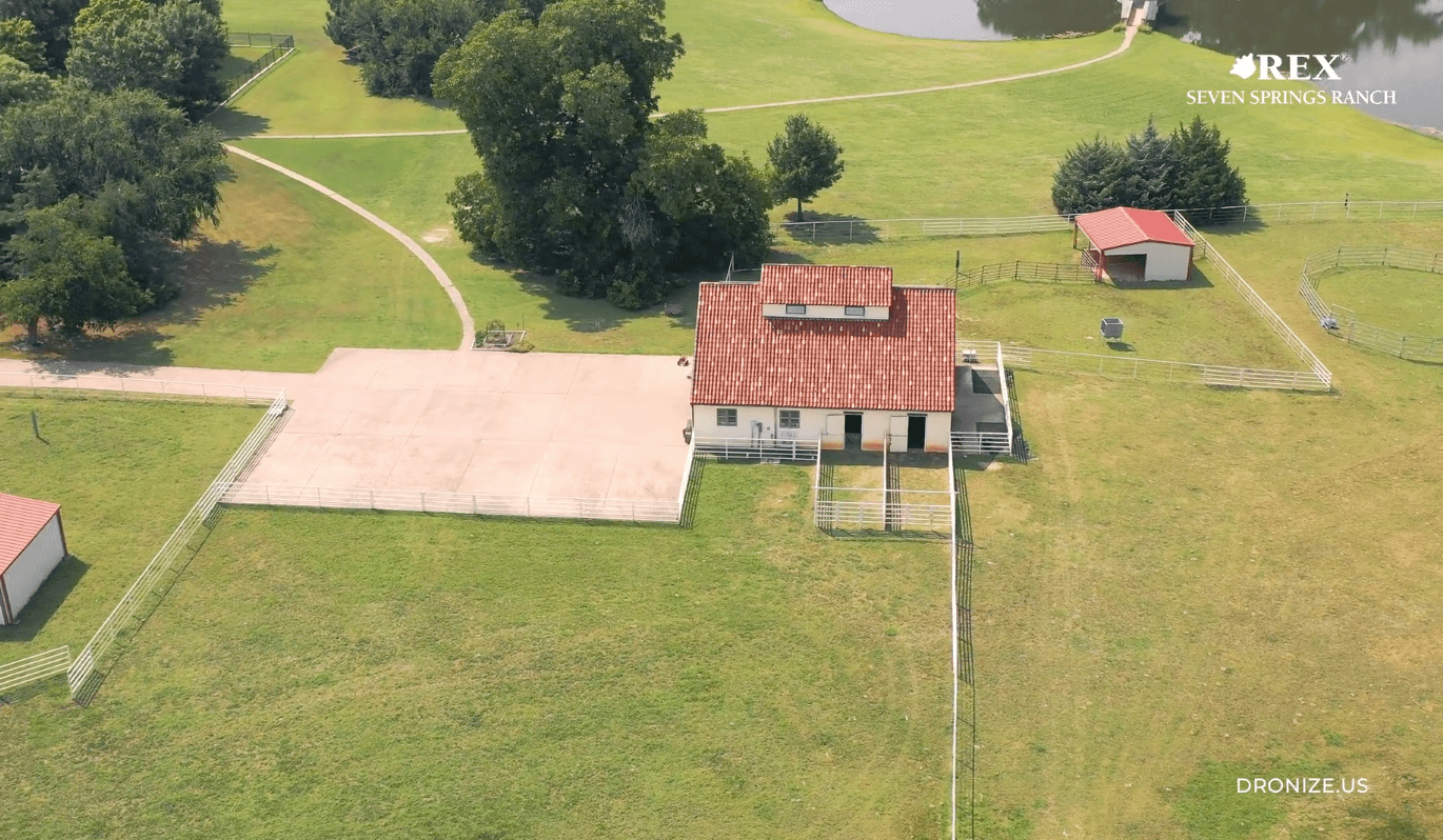 Aerial view of a ranch house with red tile roof, white walls, fenced paddocks and surrounding green fields