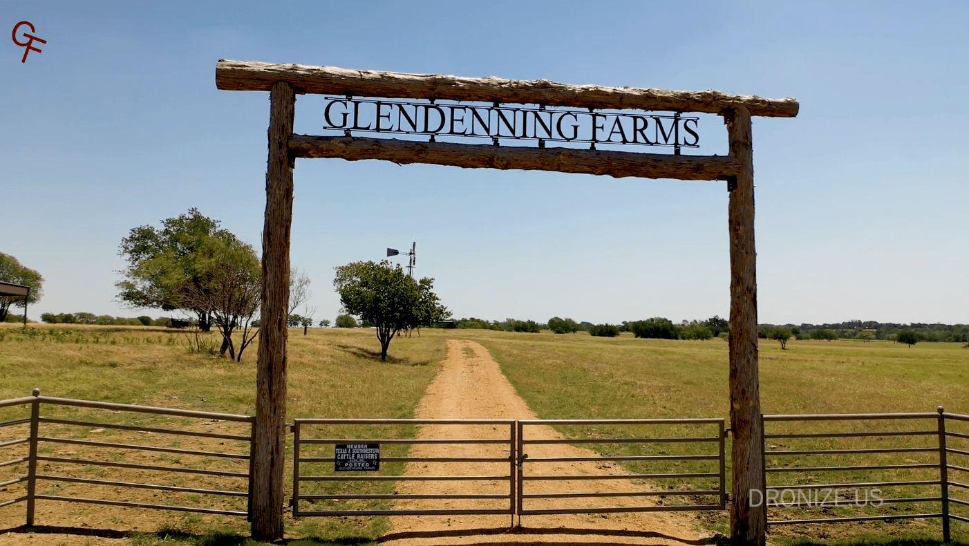 Rustic wooden gate arch with a sign reading Glendenning Farms, dirt road into open fields and trees