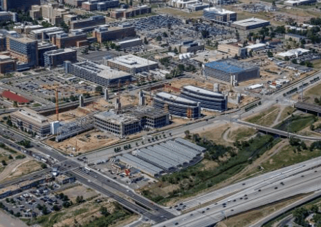 Aerial view of a construction site with cranes, surrounded by modern office buildings and a nearby highway