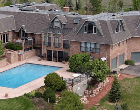 Aerial view of a two-story brick house with a rectangular blue pool in a landscaped backyard