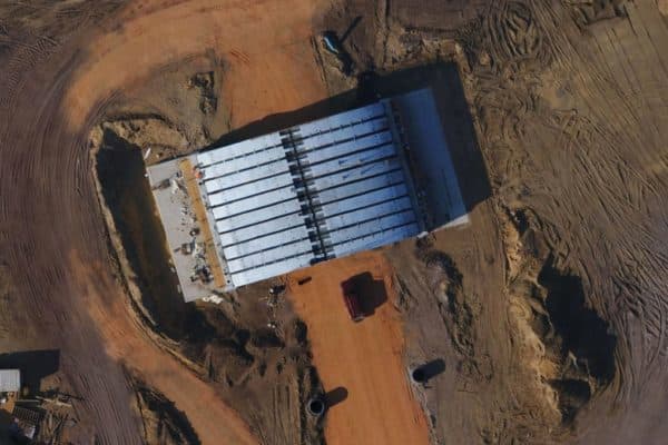 Aerial view of a construction site with a long white-roofed structure, dirt roads, and a red truck