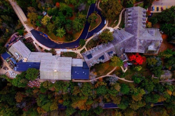 Aerial view of a large building complex with grey roofs amid dense autumn trees and winding roads