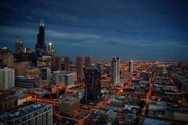 Cityscape at dusk with tall skyscrapers and illuminated streets, aerial view