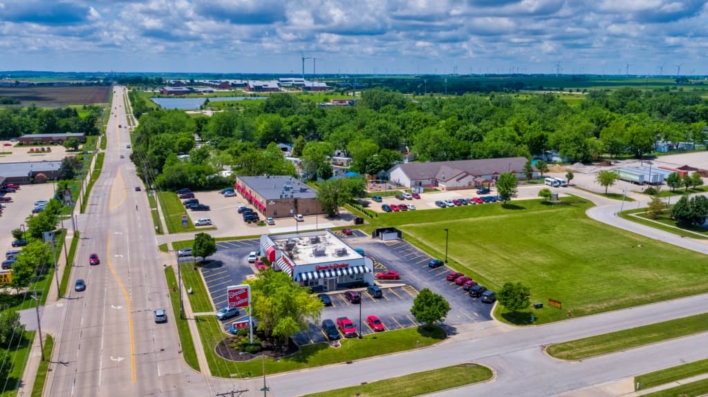 Aerial view of a commercial area with a striped building, parking lots and wind turbines in the distance
