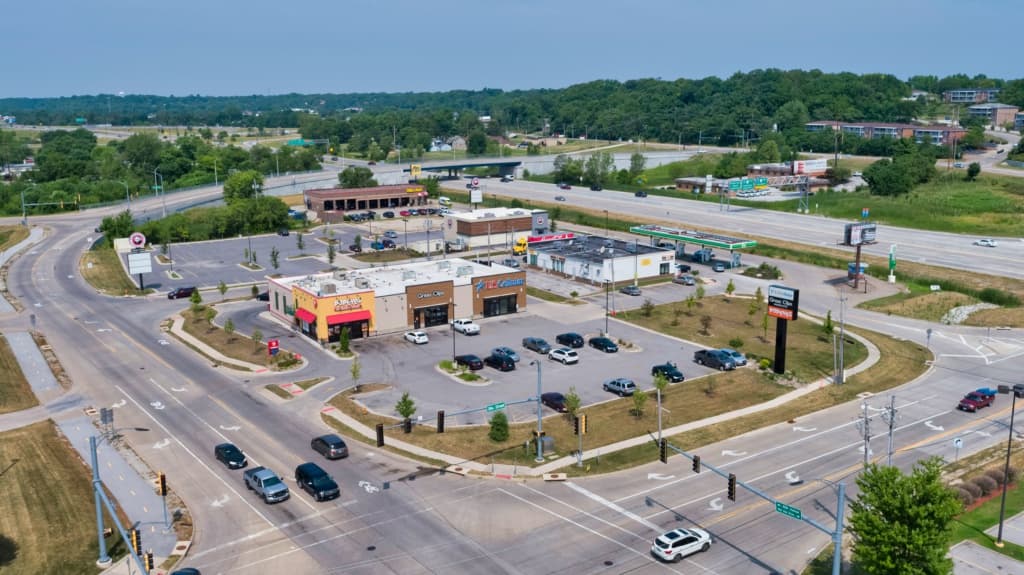 Aerial view of a shopping plaza with several storefronts, parking lots, and surrounding roads