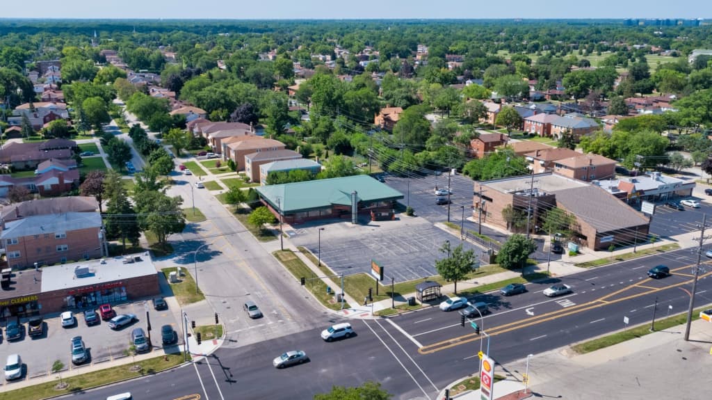 Aerial view of a suburban commercial area with a green-roofed building and parking lots