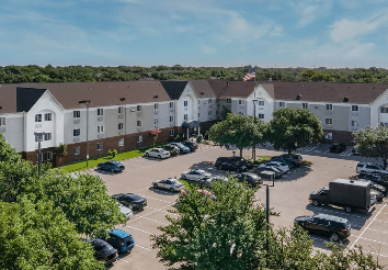 Aerial view of a residential apartment complex with a parking lot and surrounding trees