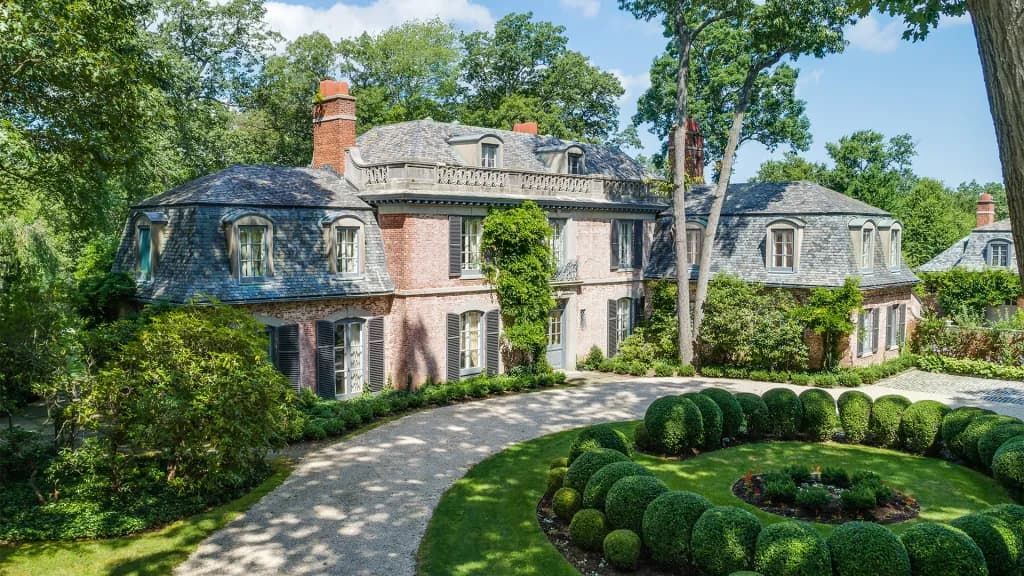 Brick mansion with slate roof and dormer windows, gravel driveway and circular hedge garden