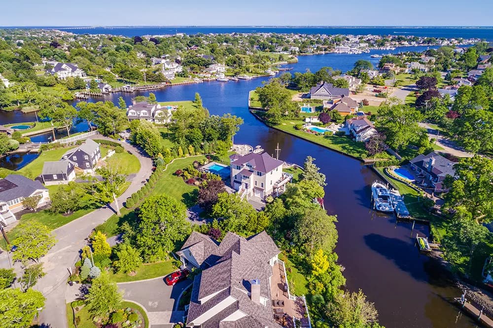 Aerial view of a canal-lined suburban neighborhood with houses, trees, and boats
