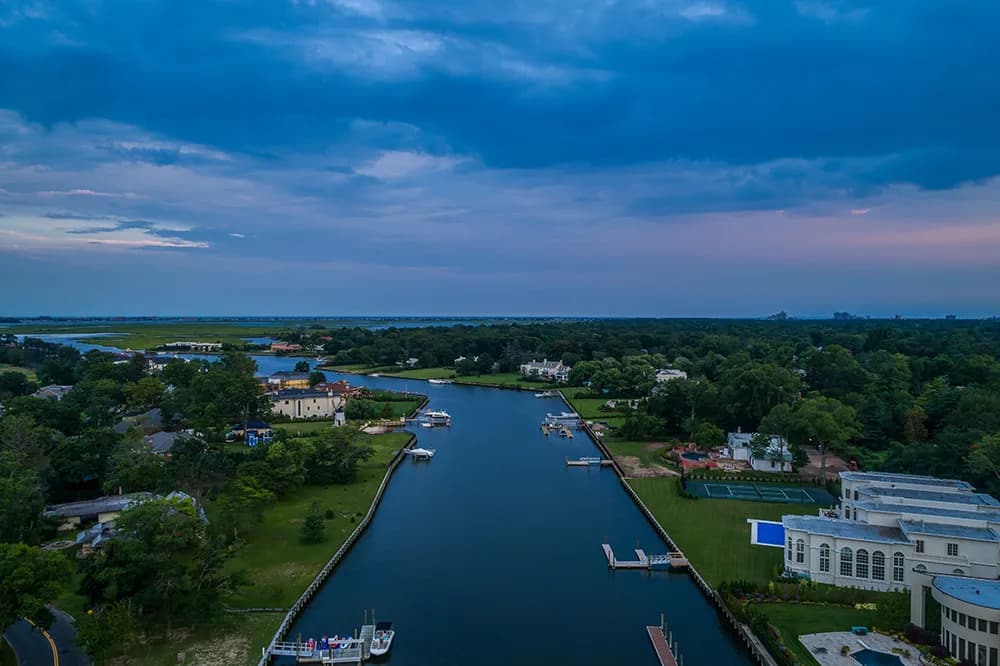 Aerial view of a canal with houses, docks, and boats on both sides, and a white building on the right