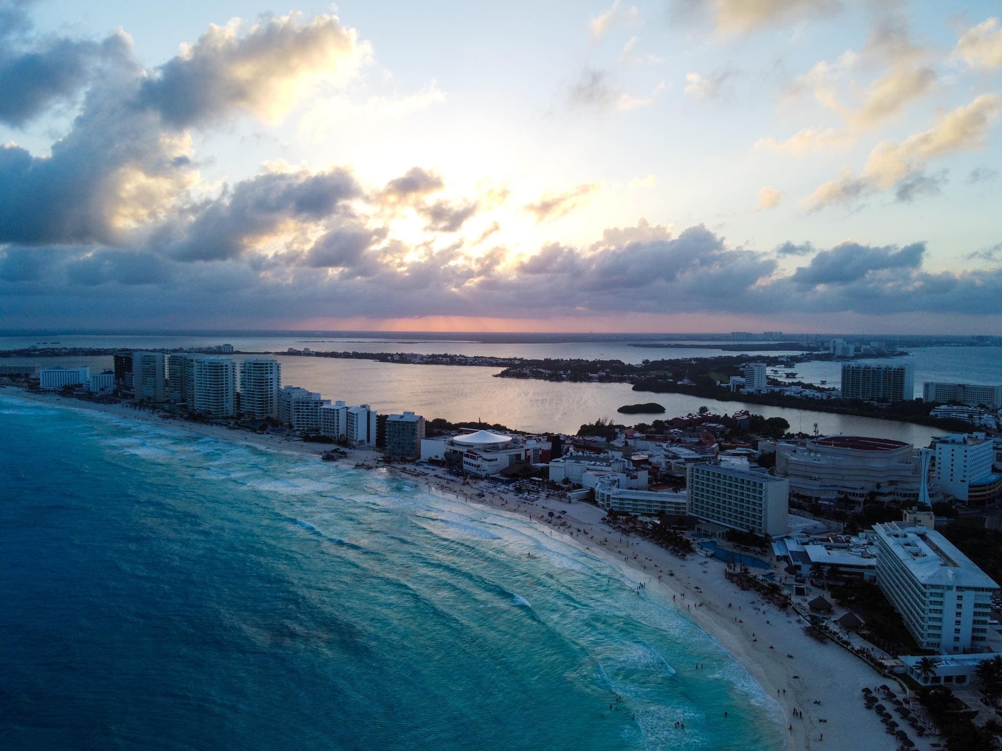 Aerial view of a coastal city with buildings along a white-sand beach and turquoise water at sunset