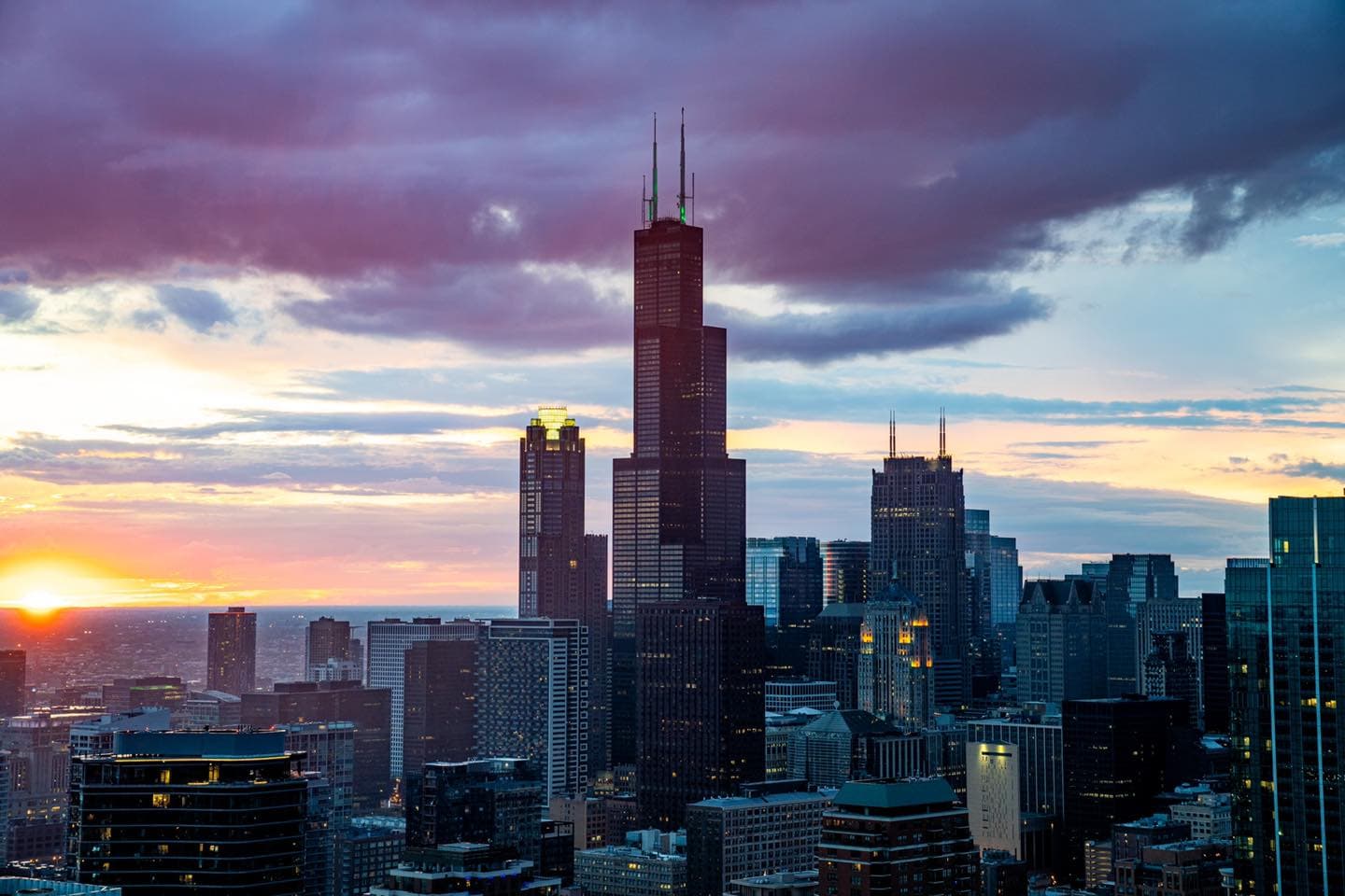 Sunset city skyline with a tall antenna-topped central skyscraper and surrounding buildings