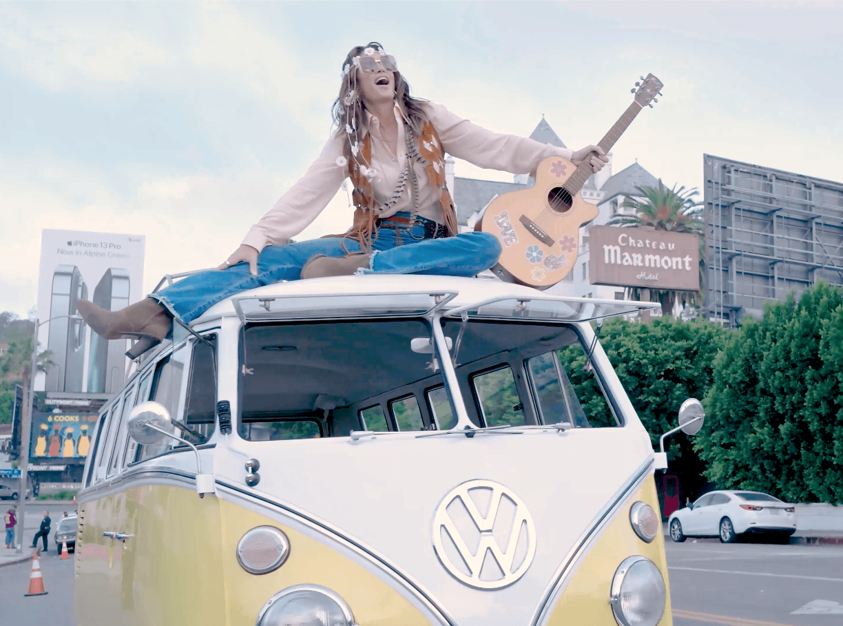 Bohemian woman sits on a vintage VW bus roof, playing a flower-decorated acoustic guitar