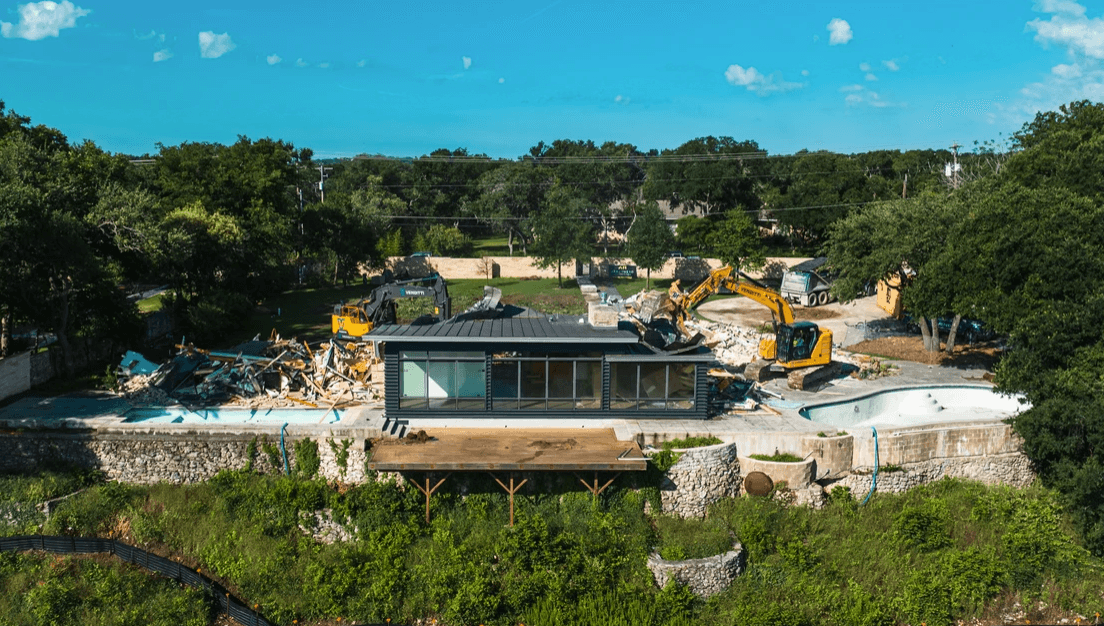 Drone view of a pool renovation with a modern glass-walled building, rubble and yellow excavators