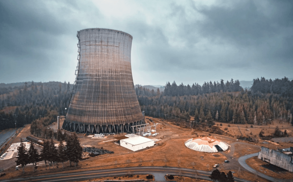 Large rust-colored cooling tower with visible support legs, surrounded by trees and small buildings