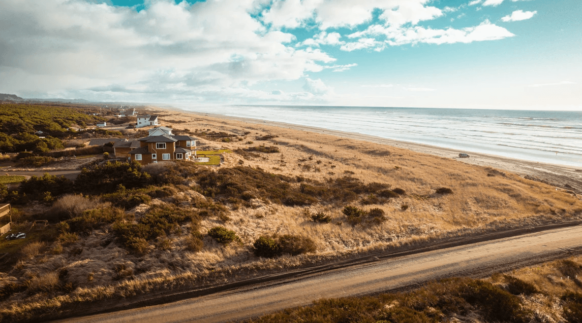 Aerial view of coastal dunes with houses, a road in the foreground, and the sea to the right