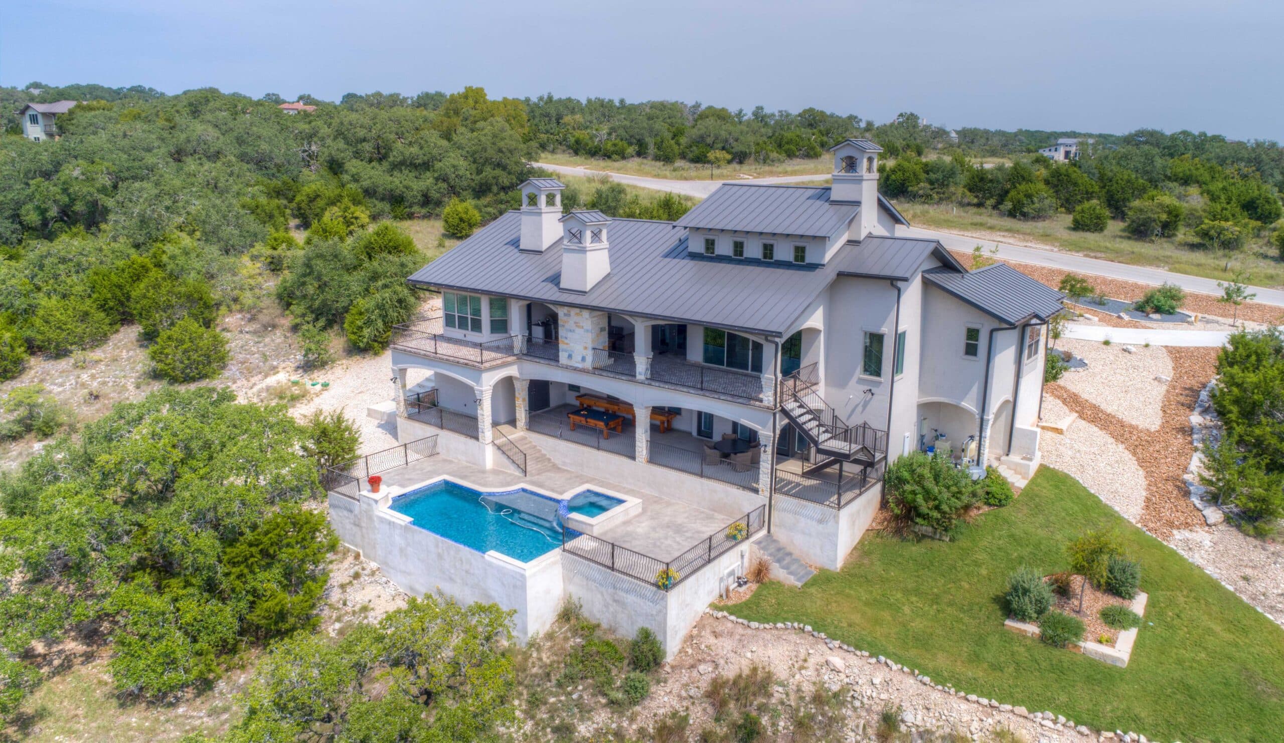 Aerial view of a modern two-story house with a gray metal roof, balconies, and a pool