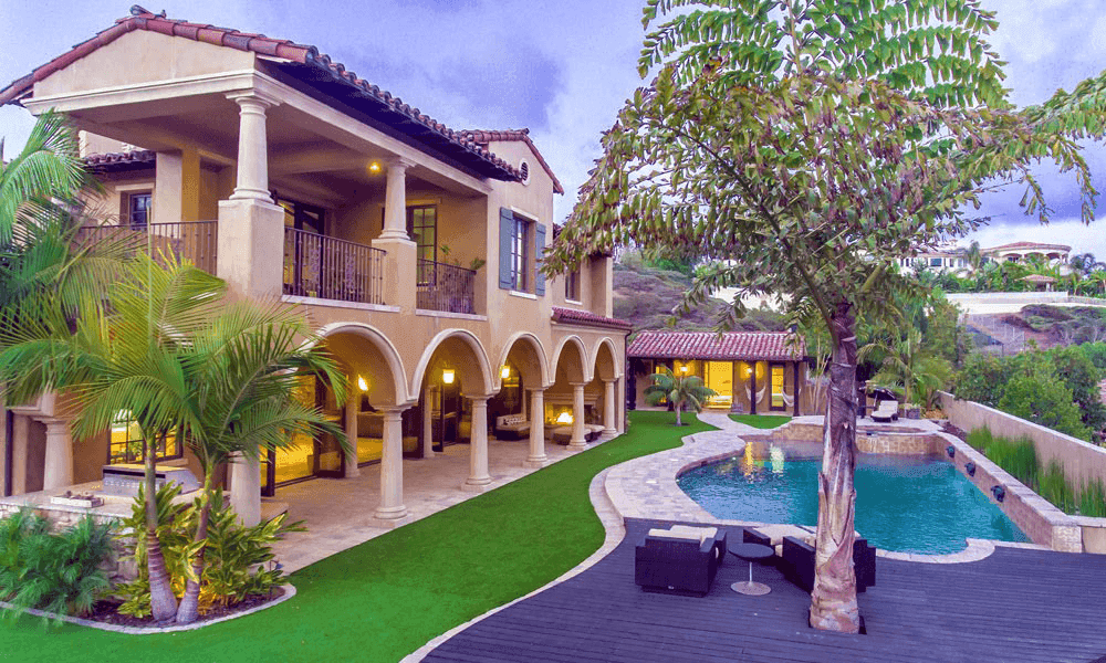 Two-story villa with arched colonnade, balcony, palm trees, and a curved pool