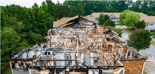 Charred house with exposed framing and scorched beams, drone shot over a suburban area