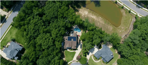 Aerial view of a suburban neighborhood with several houses among trees and a curved road, plus a blue pool