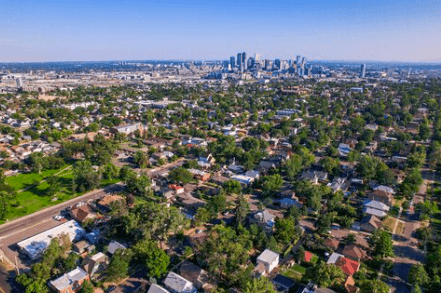 Drone aerial view of a suburban neighborhood with tree-lined streets and a distant city skyline