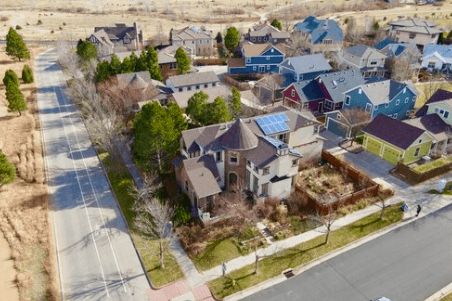 Aerial view of a suburban neighborhood with colorful houses, trees, and a central turreted house