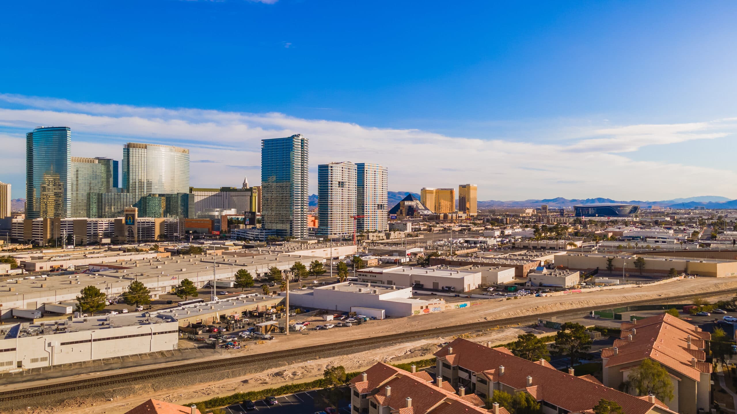 Glass skyscrapers form a city skyline under a blue sky with distant desert mountains