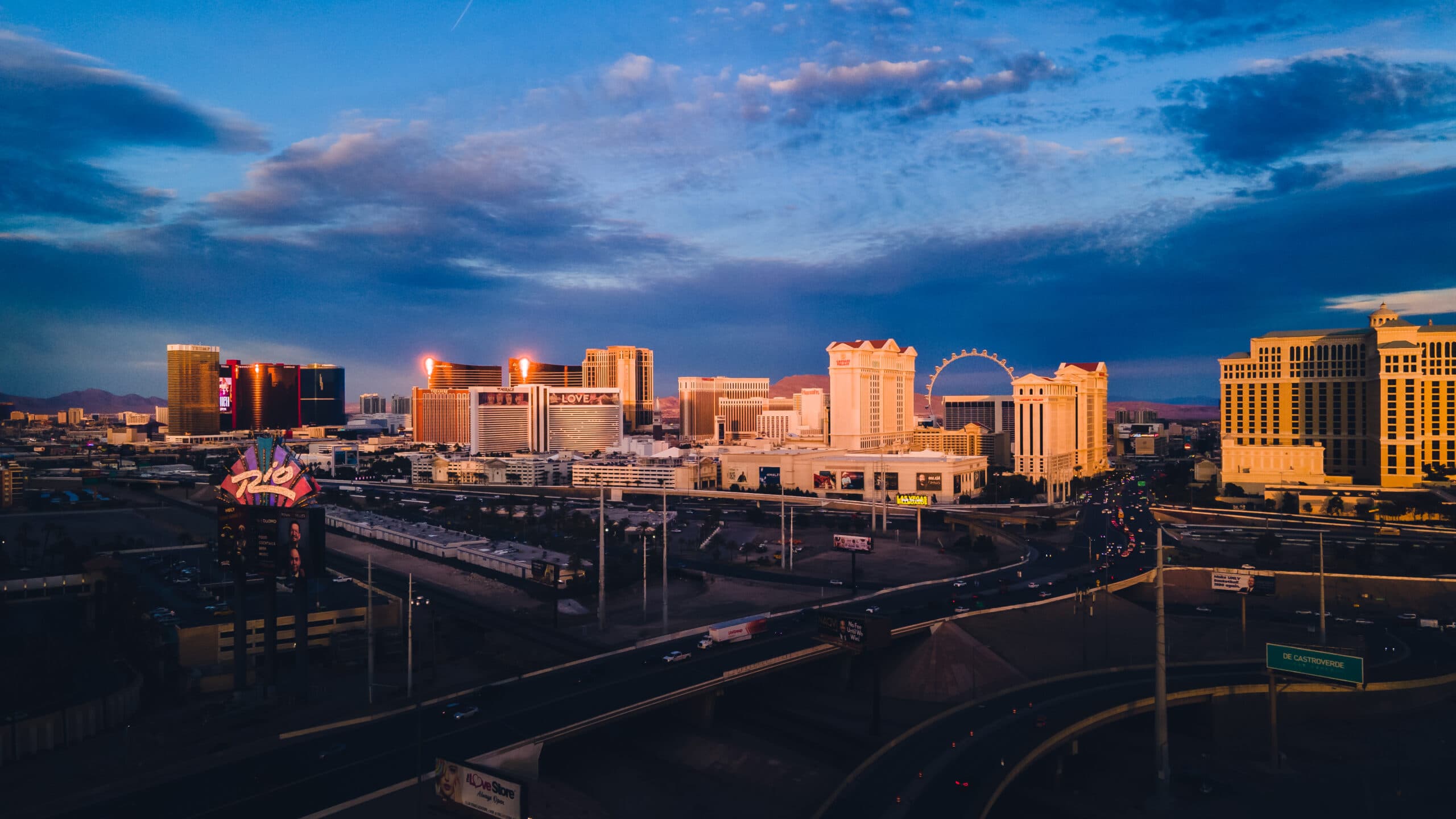Evening city skyline with tall hotels, a large Ferris wheel, and a multi-lane highway