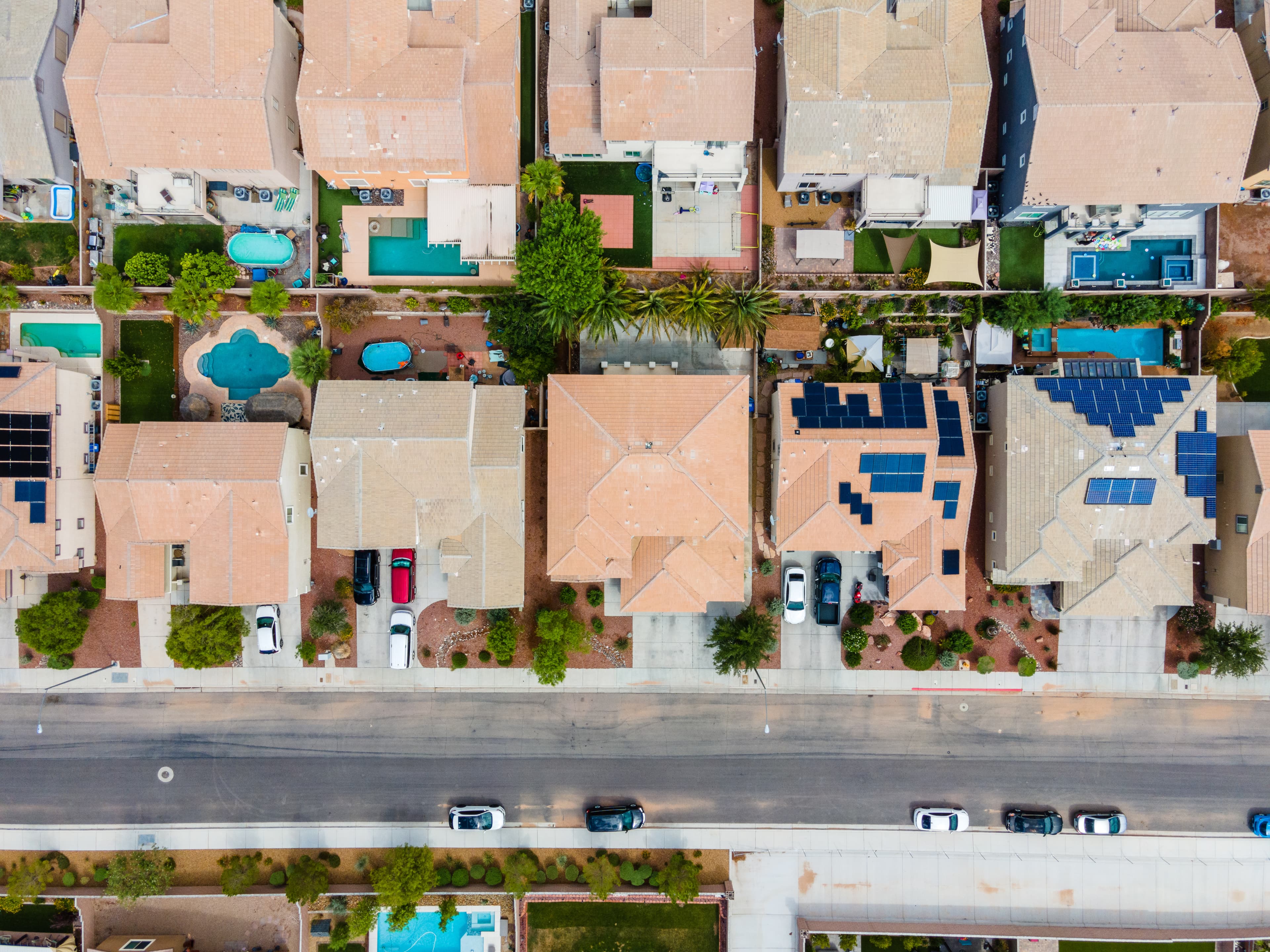 Aerial view of a suburban neighborhood with terracotta roofs, backyards with pools and solar panels