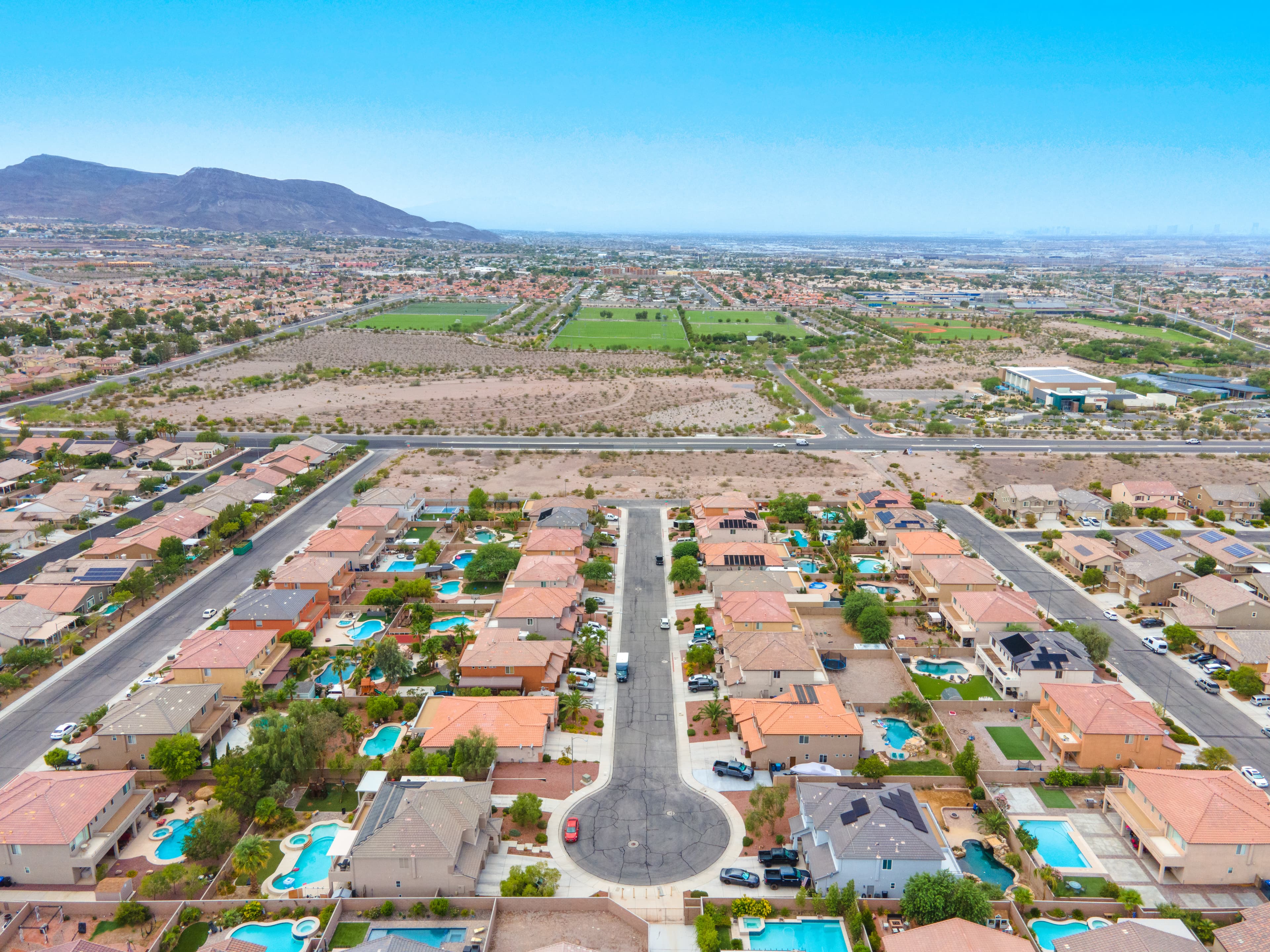 Aerial view of a suburban neighborhood with a circular cul-de-sac, houses with pools, and distant mountains