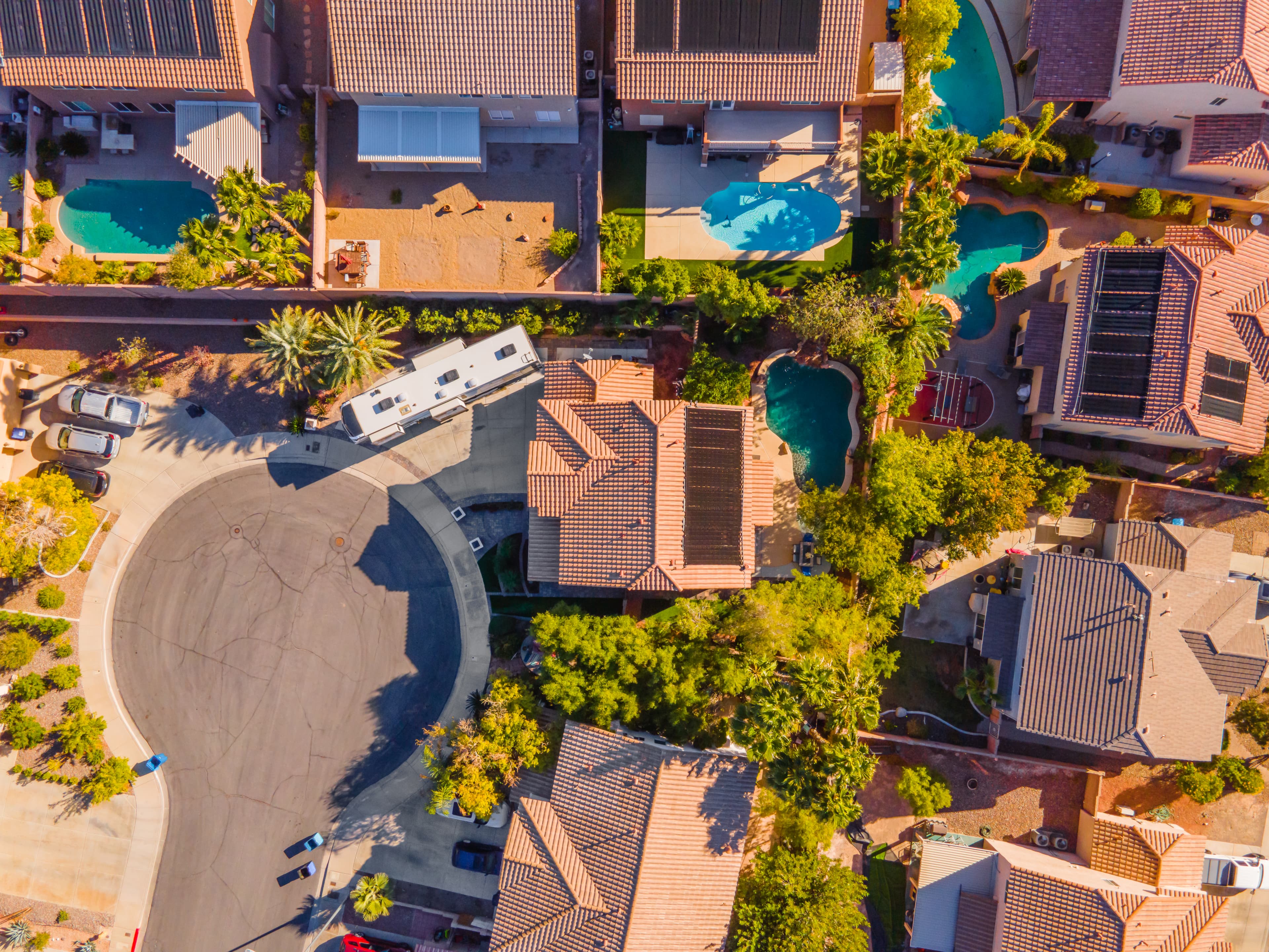 Aerial view of a suburban neighborhood with tiled roofs, circular driveway, and turquoise pools