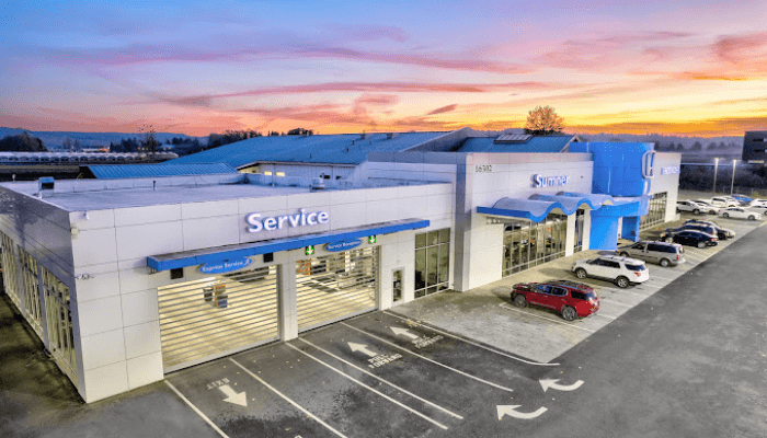 A white service center with blue accents and a large Service sign, cars parked in front under a sunset sky